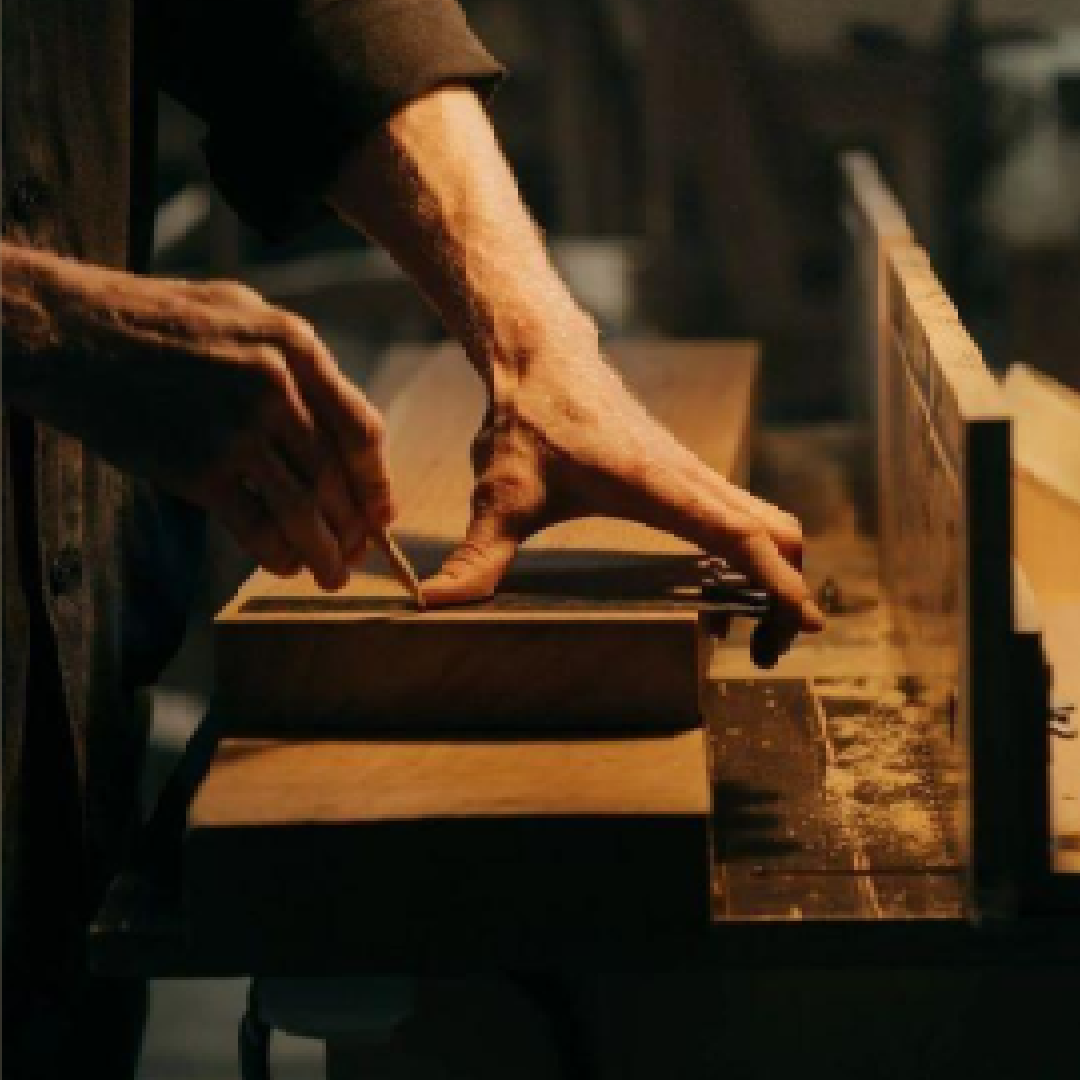 Person using a tool on a piece of wood with a warm, dimly lit background