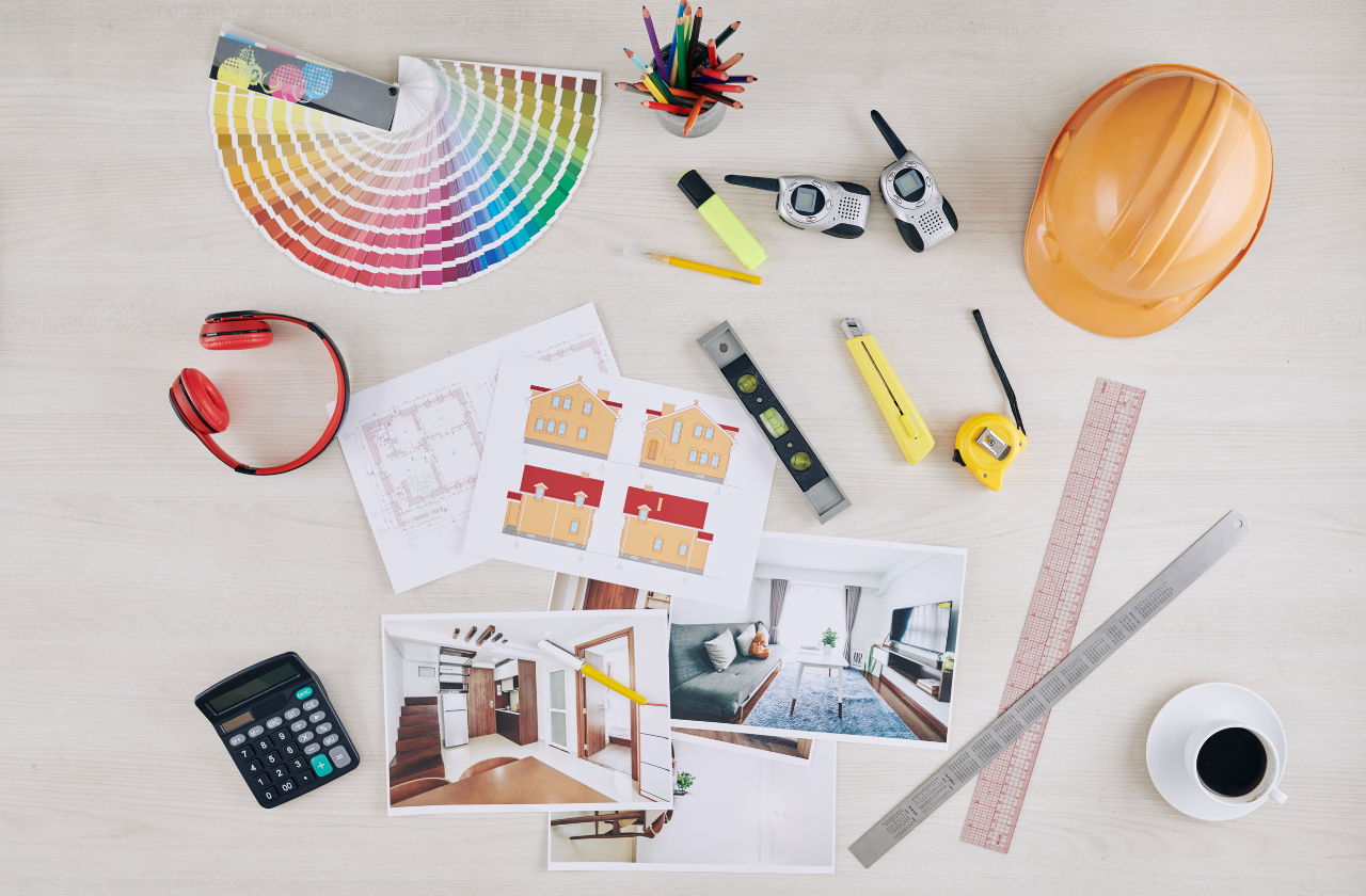 Design tools and materials on a table including a hard hat, color swatch, calculator, and architectural drawings.