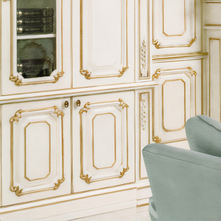 Decorative white cabinet with gold accents and a gray chair.
